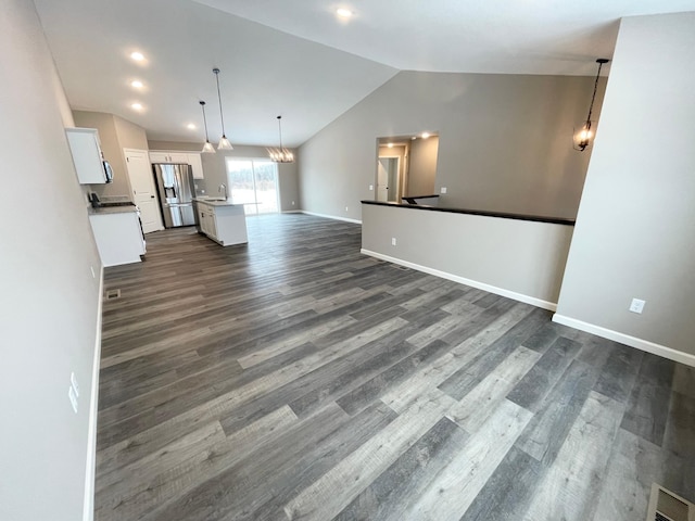 unfurnished living room with visible vents, baseboards, dark wood finished floors, an inviting chandelier, and vaulted ceiling