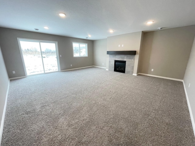 unfurnished living room with a textured ceiling, a tile fireplace, recessed lighting, carpet flooring, and baseboards