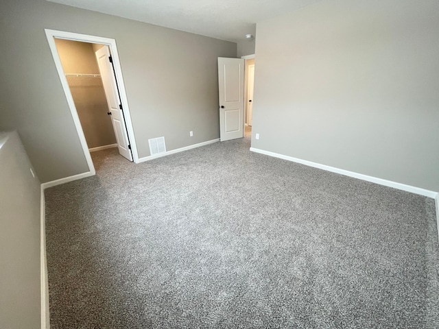 unfurnished bedroom with a walk in closet, carpet, visible vents, and baseboards