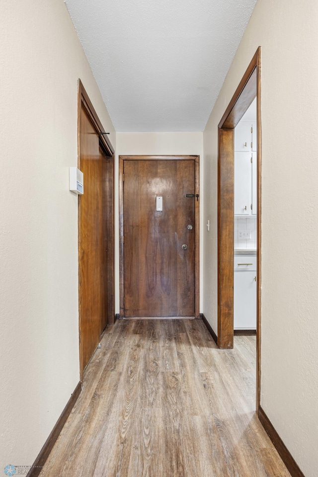 corridor featuring light wood-type flooring and baseboards