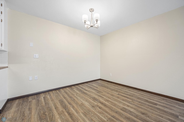 spare room with a notable chandelier, baseboards, and wood finished floors