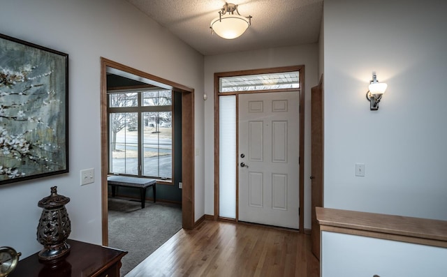 foyer entrance with light wood-style floors, baseboards, and a textured ceiling