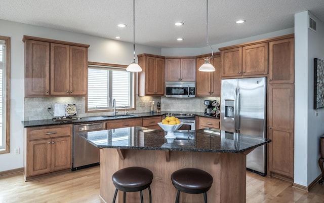 kitchen with a center island, visible vents, appliances with stainless steel finishes, brown cabinetry, and a sink