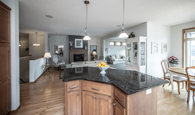 kitchen featuring hanging light fixtures, light wood-style flooring, dark stone countertops, and a glass covered fireplace