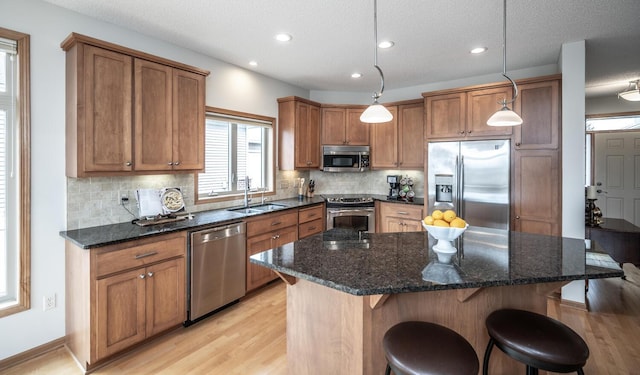 kitchen featuring light wood finished floors, appliances with stainless steel finishes, brown cabinetry, a sink, and a kitchen bar