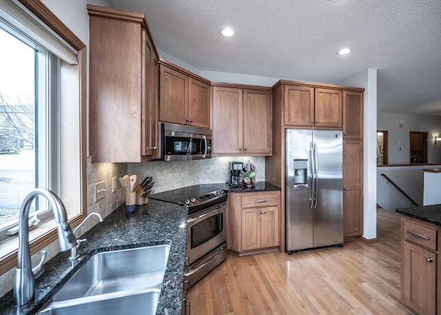 kitchen featuring stainless steel appliances, a sink, light wood-type flooring, decorative backsplash, and dark stone countertops