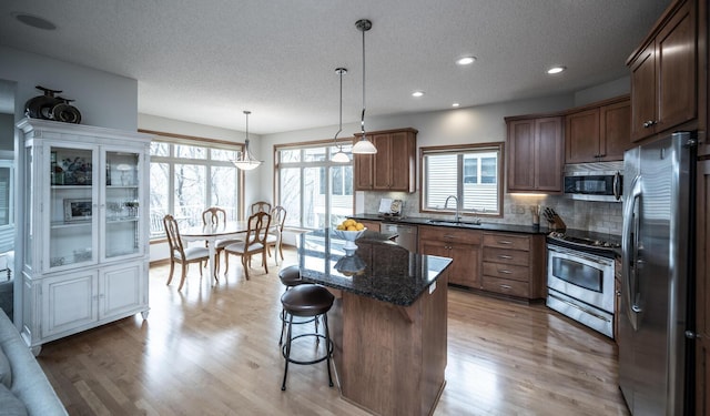 kitchen with light wood finished floors, a kitchen island, stainless steel appliances, a kitchen bar, and a sink