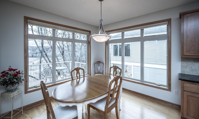 dining space featuring light wood-style floors, baseboards, visible vents, and a textured ceiling