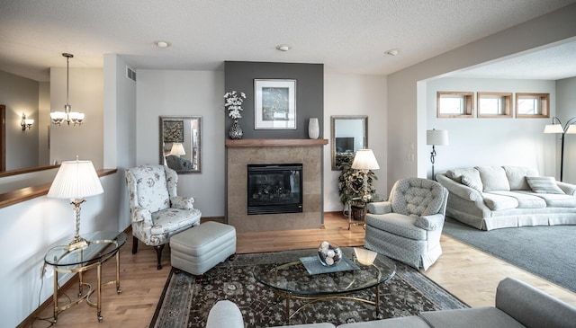 living area featuring visible vents, wood finished floors, a textured ceiling, a fireplace, and a chandelier