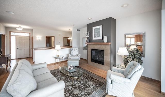 living room with a textured ceiling, a fireplace, wood finished floors, visible vents, and baseboards