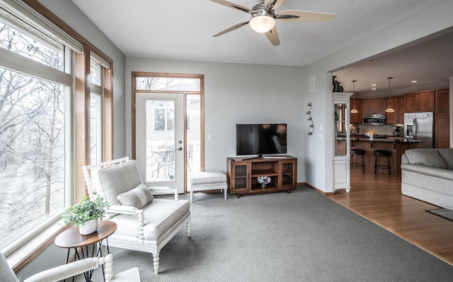 carpeted living room with ceiling fan, a textured ceiling, a wealth of natural light, and baseboards