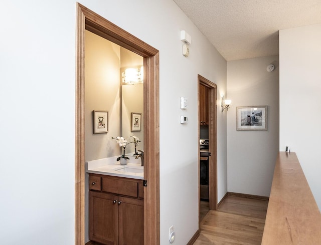 hall with a textured ceiling, light wood-type flooring, a sink, and baseboards