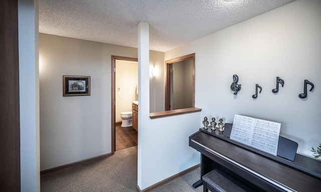 corridor with a textured ceiling, carpet, and baseboards