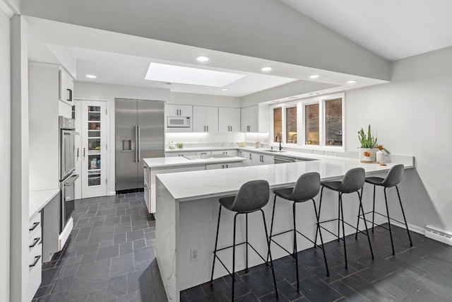 kitchen with recessed lighting, a peninsula, a kitchen breakfast bar, and built in appliances