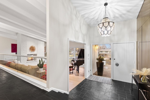 foyer featuring a chandelier, stone tile floors, a high ceiling, baseboards, and beam ceiling