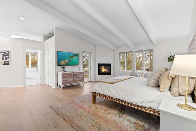 bedroom with lofted ceiling with beams, multiple windows, light wood-type flooring, and connected bathroom