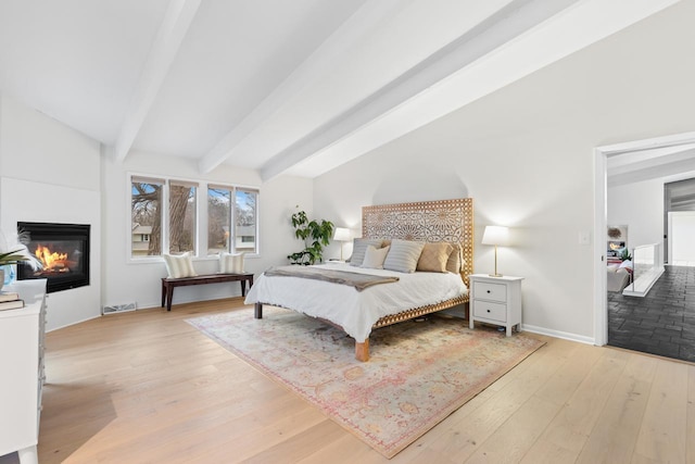 bedroom featuring vaulted ceiling with beams, light wood finished floors, visible vents, and a glass covered fireplace