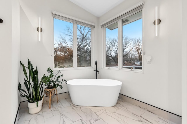 full bath featuring lofted ceiling, marble finish floor, a soaking tub, and baseboards