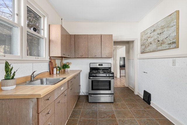 kitchen with visible vents, baseboards, stainless steel range with gas stovetop, ornamental molding, and a sink