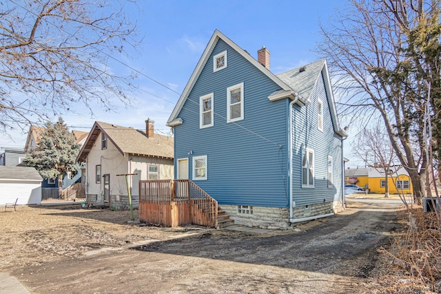 back of property with driveway, a chimney, and a shingled roof