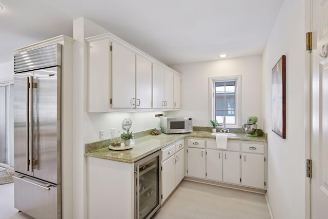 kitchen featuring white microwave, a sink, wine cooler, white cabinets, and built in refrigerator