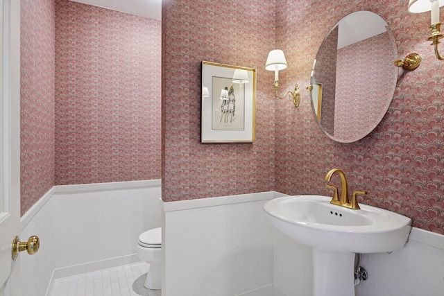 half bath featuring tile patterned flooring, a wainscoted wall, and wallpapered walls