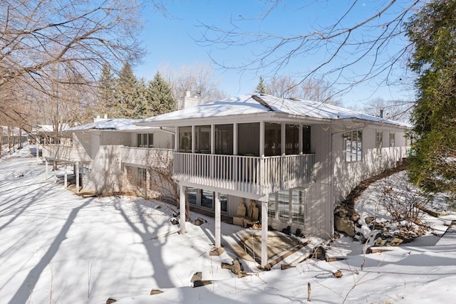 snow covered property with a chimney and a sunroom