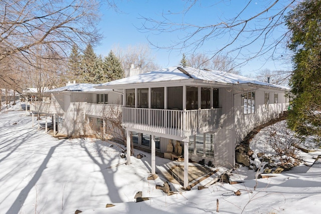 snow covered rear of property with a chimney and a sunroom