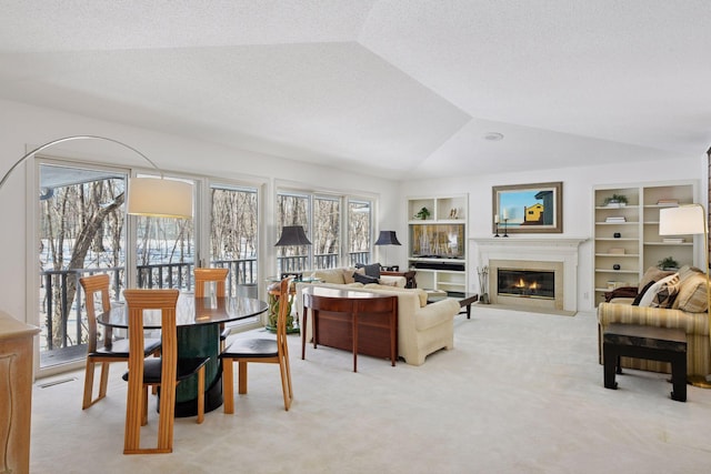 living area with a glass covered fireplace, built in shelves, vaulted ceiling, and light carpet