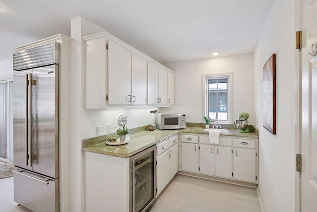 kitchen with beverage cooler, white microwave, built in fridge, light wood finished floors, and white cabinetry