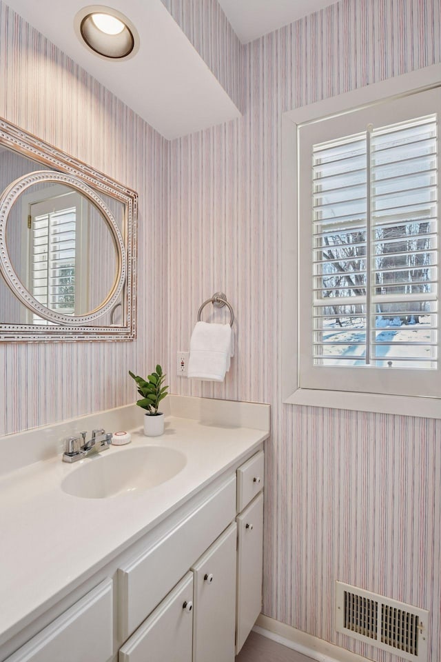 bathroom featuring visible vents, vanity, wallpapered walls, and baseboards
