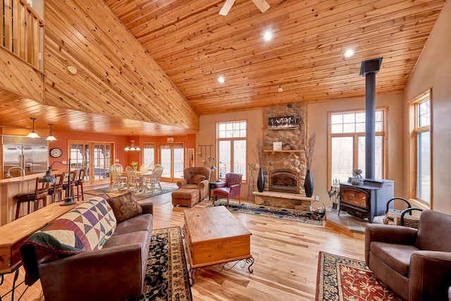 living area with wood-type flooring, wood ceiling, a wood stove, ceiling fan, and high vaulted ceiling