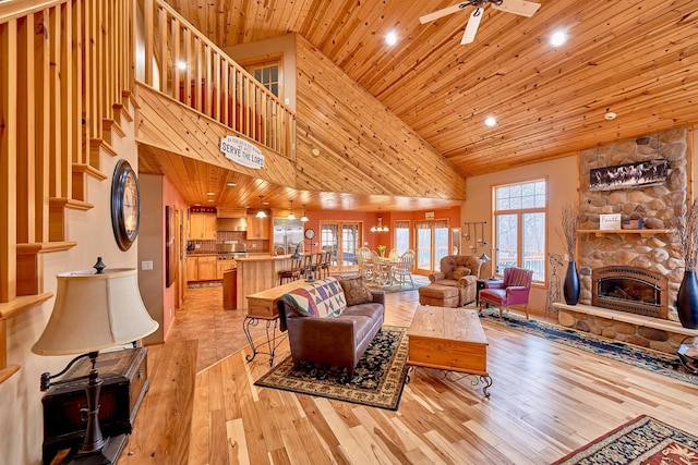 living area featuring a ceiling fan, wood ceiling, a stone fireplace, light wood-type flooring, and high vaulted ceiling