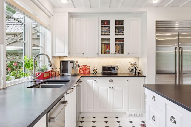 kitchen featuring appliances with stainless steel finishes, dark countertops, white cabinetry, and a sink