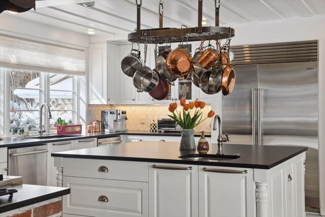 kitchen with stainless steel appliances, dark countertops, decorative backsplash, white cabinets, and a sink