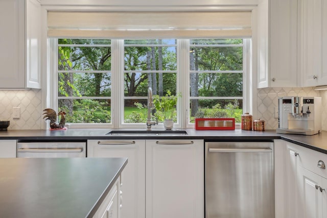 kitchen with stainless steel dishwasher, dark countertops, a sink, and white cabinets