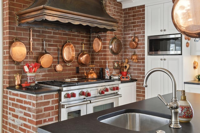 kitchen featuring white cabinets, dark countertops, custom exhaust hood, stainless steel appliances, and a sink