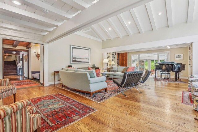 living room with baseboards, vaulted ceiling with beams, stairway, and light wood finished floors