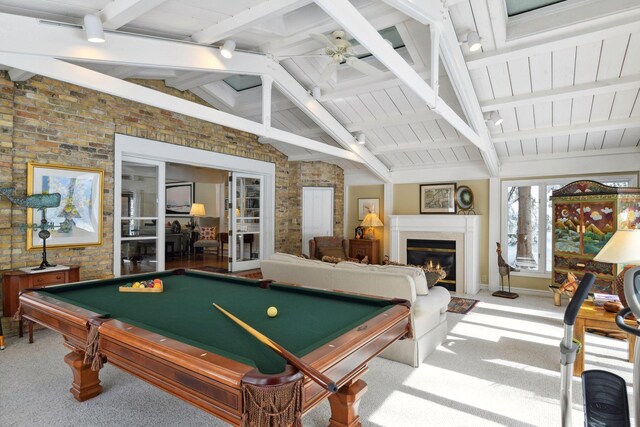 playroom with a glass covered fireplace, lofted ceiling with beams, brick wall, ceiling fan, and carpet floors