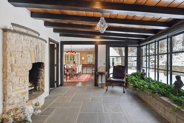 unfurnished sunroom with wooden ceiling, an inviting chandelier, beam ceiling, and a stone fireplace