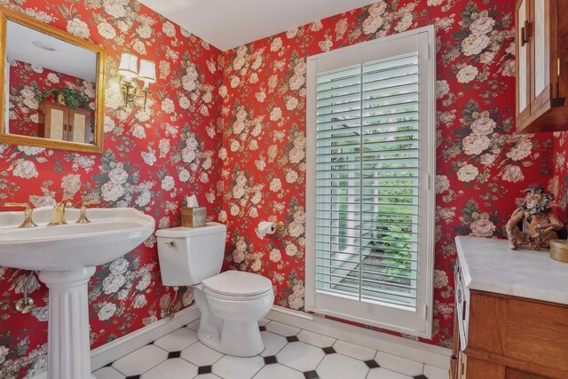 half bath with toilet, wallpapered walls, baseboards, and a sink