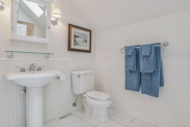 half bathroom with a wainscoted wall, tile patterned flooring, visible vents, and vaulted ceiling