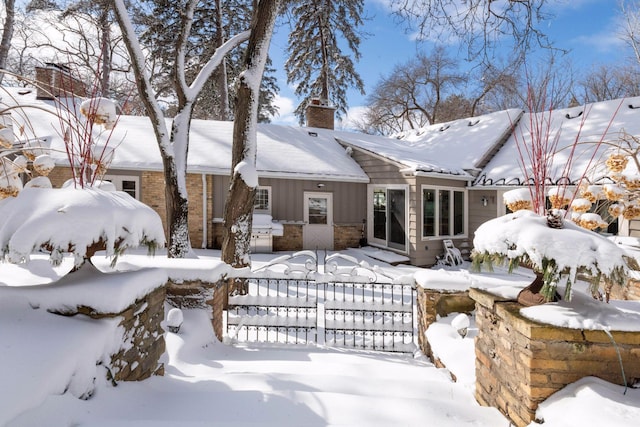 snow covered house with a garage, brick siding, a chimney, and board and batten siding