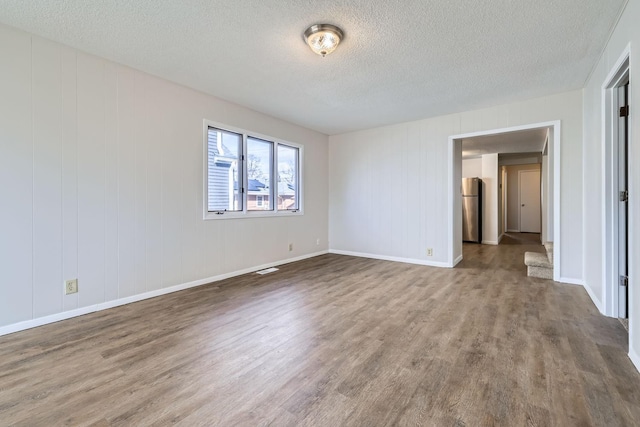 unfurnished bedroom with a textured ceiling, wood finished floors, freestanding refrigerator, and baseboards