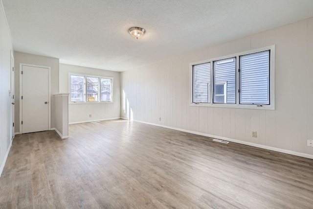 empty room featuring visible vents, a textured ceiling, baseboards, and wood finished floors