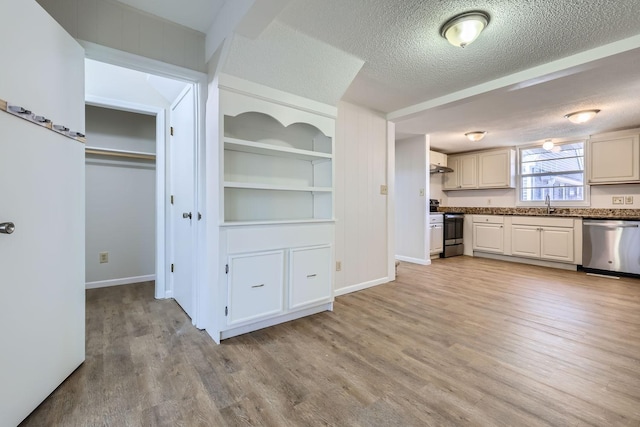 kitchen with dark countertops, stainless steel appliances, a textured ceiling, light wood-style floors, and a sink