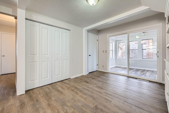 unfurnished bedroom featuring a closet, a textured ceiling, baseboards, and wood finished floors