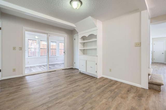 unfurnished living room featuring built in shelves, a textured ceiling, and wood finished floors