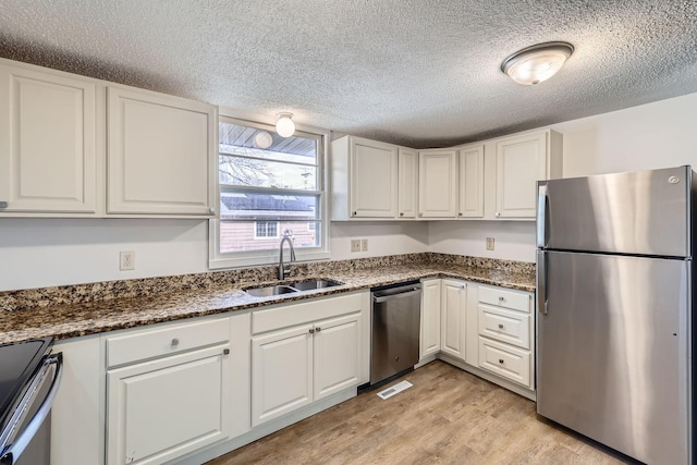 kitchen featuring visible vents, light wood-style flooring, stainless steel appliances, white cabinetry, and a sink