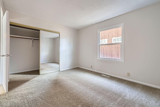 unfurnished bedroom featuring baseboards, visible vents, carpet, a textured ceiling, and a closet